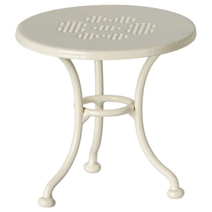 Das Maileg Café-Set besteht aus einem cremefarbenen Metalltisch mit einem runden, perforierten Blumenmuster auf der Oberseite und drei elegant geschwungenen Beinen.