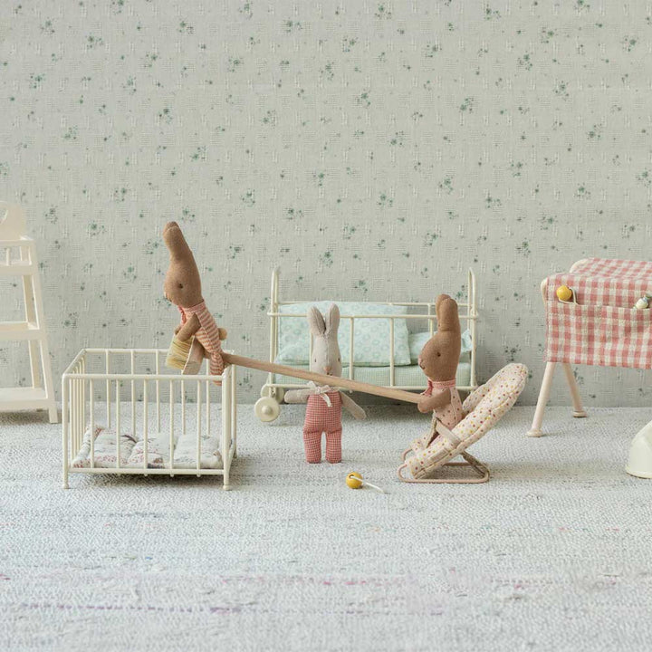 Das Maileg - Hase Rabbit MY Set enthält drei Spielzeugkaninchen in einem Miniaturkinderzimmer, komplett mit Krippen und Stuhl. Ein Kaninchen balanciert spielerisch auf einem Gitterbett.