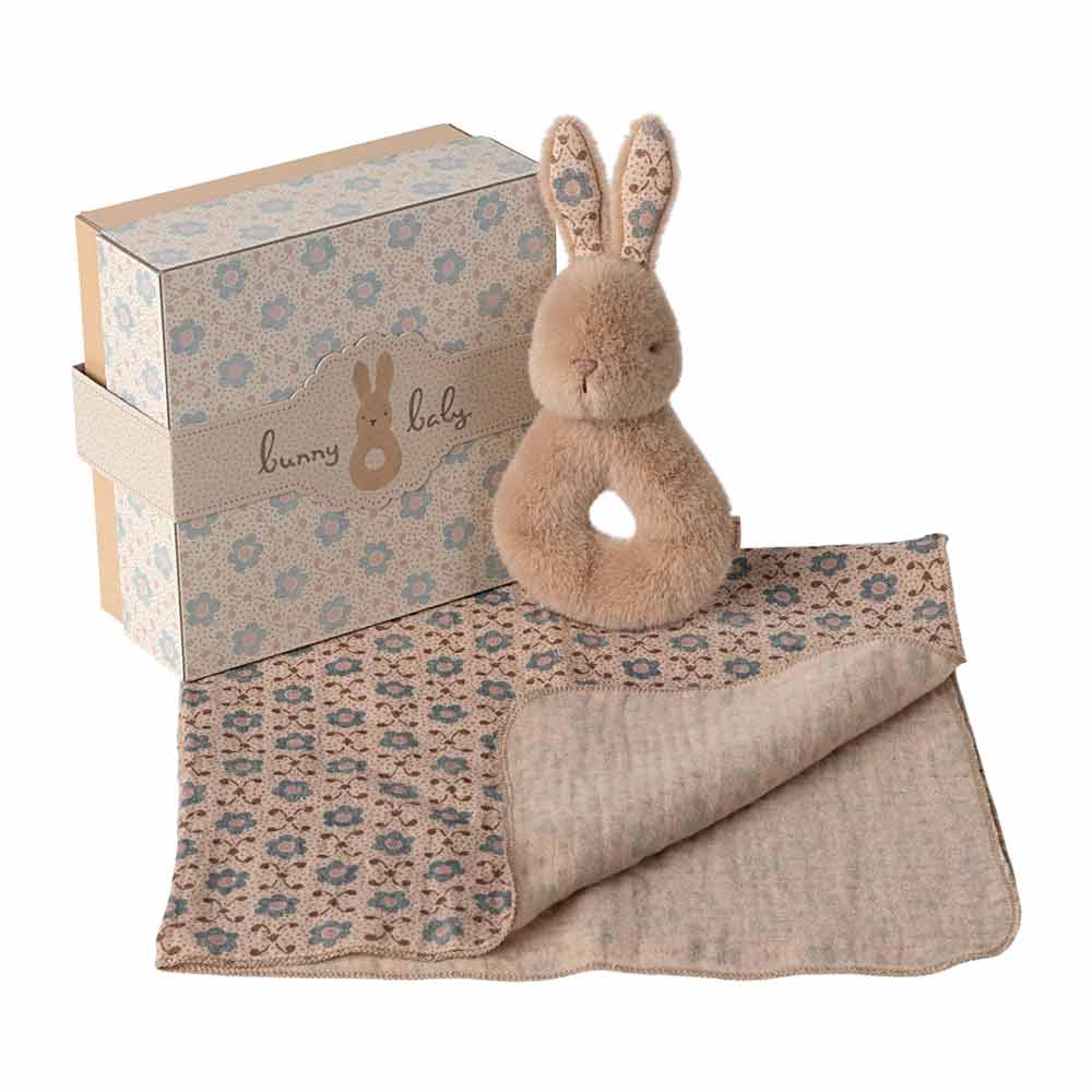 Das Maileg - Hase Rassel-Set Creme Pfirsich ist ein Geschenkset mit einer gemusterten Schachtel, einer plüschigen Hasenrassel und einer dazu passenden gestrickten Babydecke in Beige- und Blautönen.