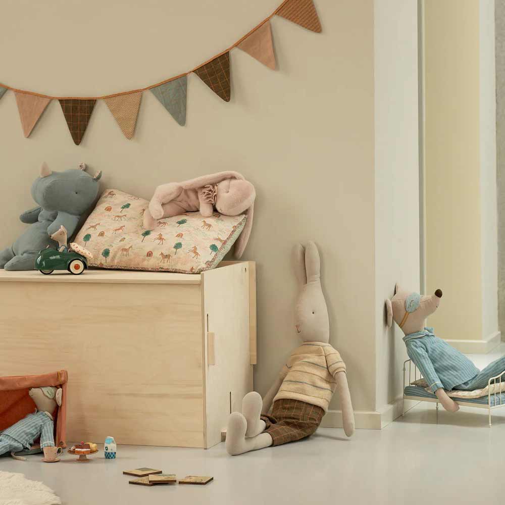 Ein gemütliches Kinderzimmer mit Plüschtieren, einer Spielzeugkiste aus Holz, dem Maileg Kissen Einhorn und einer Wimpelkette an der Wand. Auf dem Boden liegen Bauklötze und Bücher verstreut.