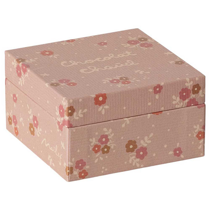 Eine rosafarbene, quadratische Geschenkbox, verziert mit Blumenmustern und dem Text „Chocolat Cheval“ auf dem Deckel, bekannt als Maileg – Miniatur Heiße Schokolade Set.