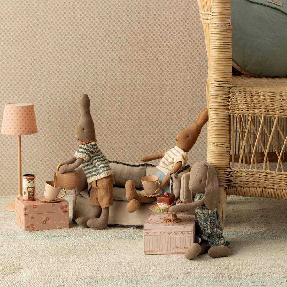 Miniatur-Stoffhasen in lässiger Kleidung genießen eine Teeparty auf einem Sofa und einem Sessel, begleitet vom Maileg Miniatur Heiße Schokolade Set und einem Spielzeugkuchen.