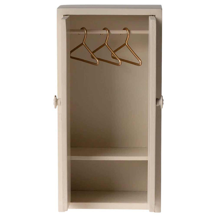 Maileg - Miniatur-Kleiderschrank Maus in Beige verfügt über eine offene Tür, drei goldene Kleiderbügel an einer Stange und zwei Regale unten.
