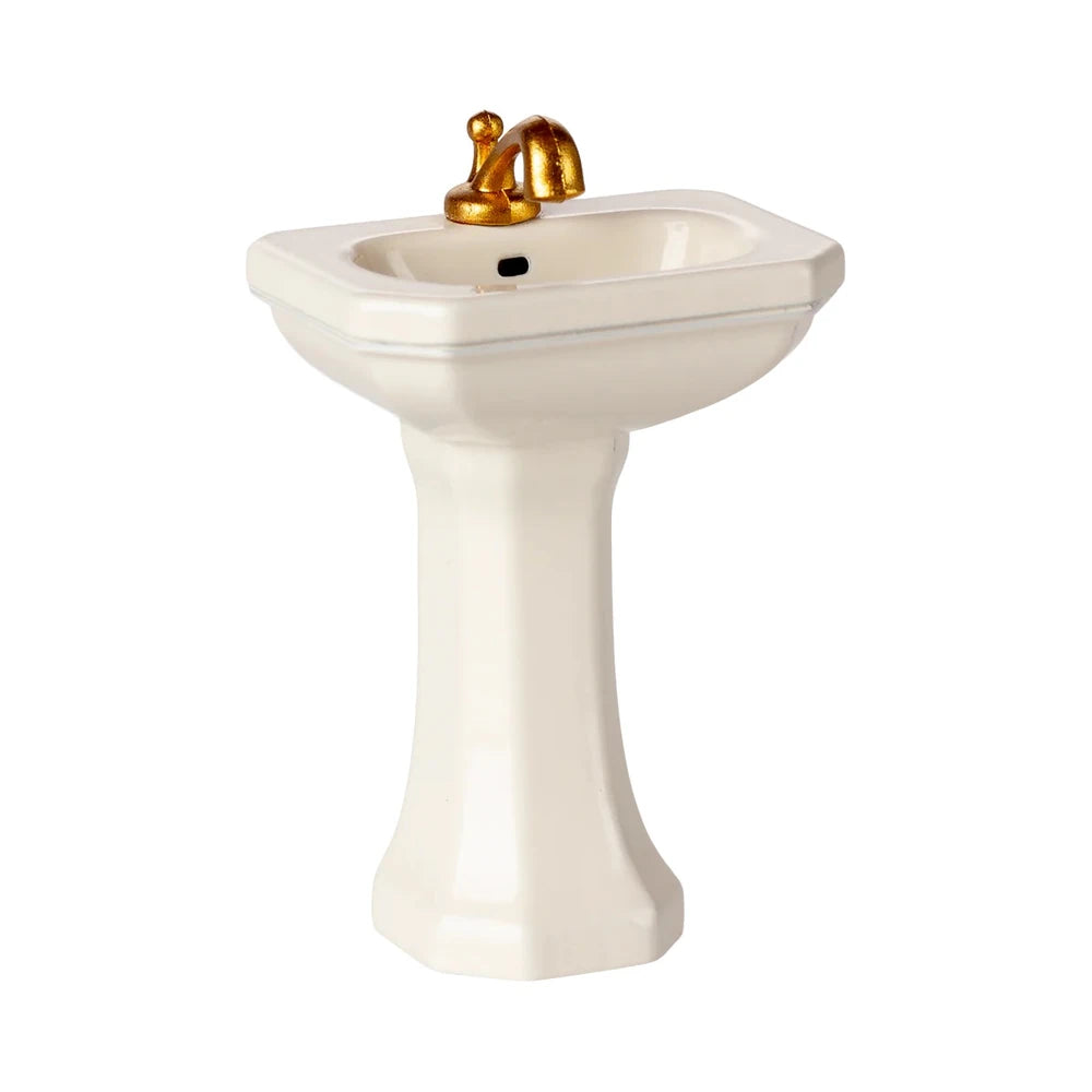 Das Maileg - Miniatur Waschbecken Maus White ist ein kleines weißes Sockelbecken mit einem goldenen Wasserhahn und einem einzigen Abflussloch, das vor einem schlichten weißen Hintergrund steht.