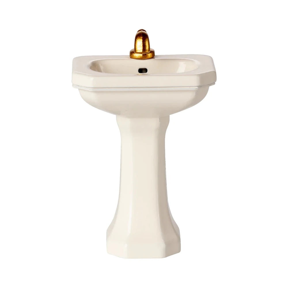 Das Maileg Miniatur Waschbecken Maus White ist ein kleines, weißes Sockelwaschbecken mit einem goldenen Wasserhahn, der vor einem schlichten weißen Hintergrund steht.