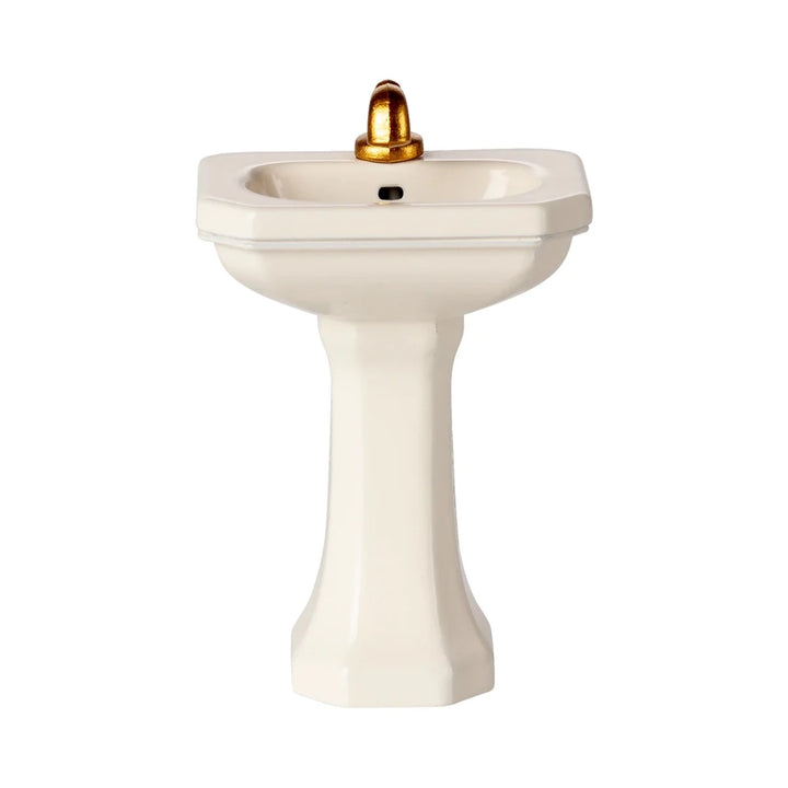 Das Maileg Miniatur Waschbecken Maus White ist ein kleines, weißes Sockelwaschbecken mit einem goldenen Wasserhahn, der vor einem schlichten weißen Hintergrund steht.