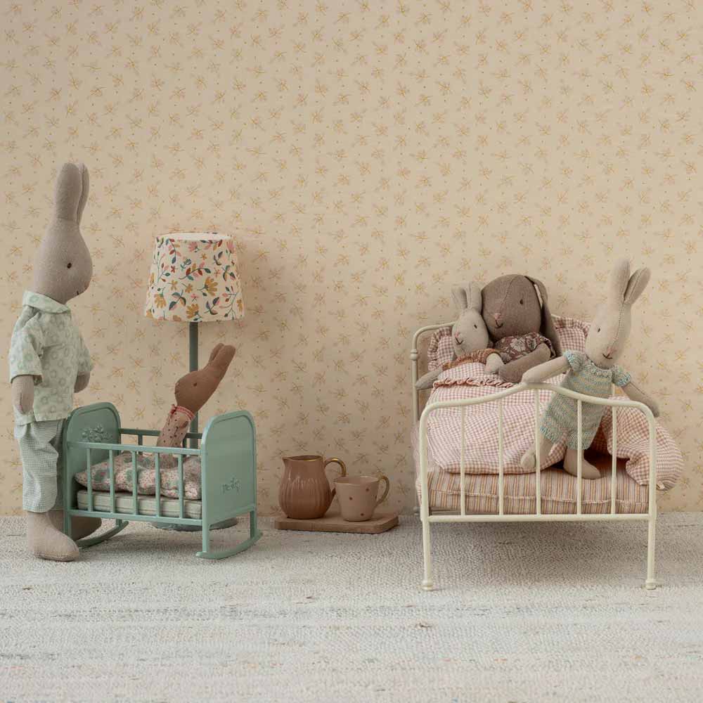 Eine Kinderzimmerszene mit Mailegs Puppenmöbeln Wiege My hat Stoffhasen; ein Hase steht neben der Wiege, während andere auf dem Bett sitzen. Auf dem Boden steht ein Teeservice.