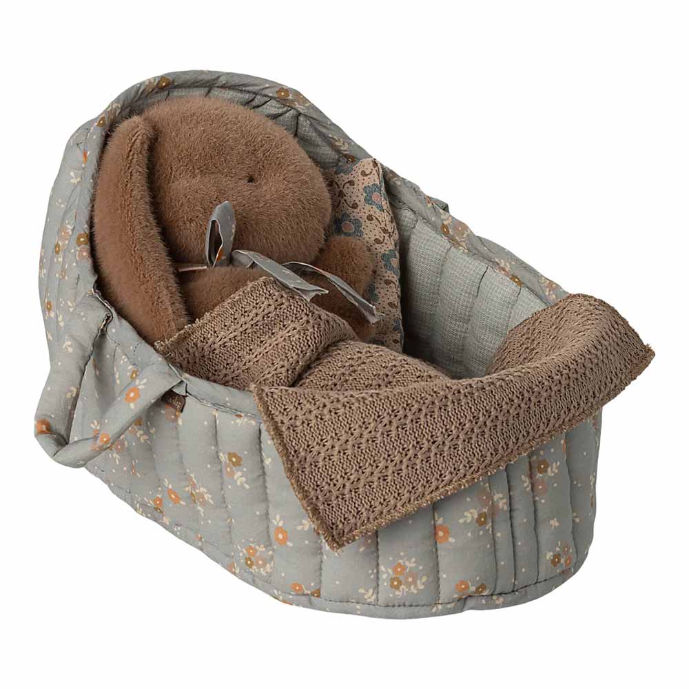 Die Maileg - Tragetasche Groß ist eine weich gepolsterte Puppentasche mit einer braunen Decke und einem Plüschbären im Inneren, die außen mit einem grauen Blumenmuster versehen ist.