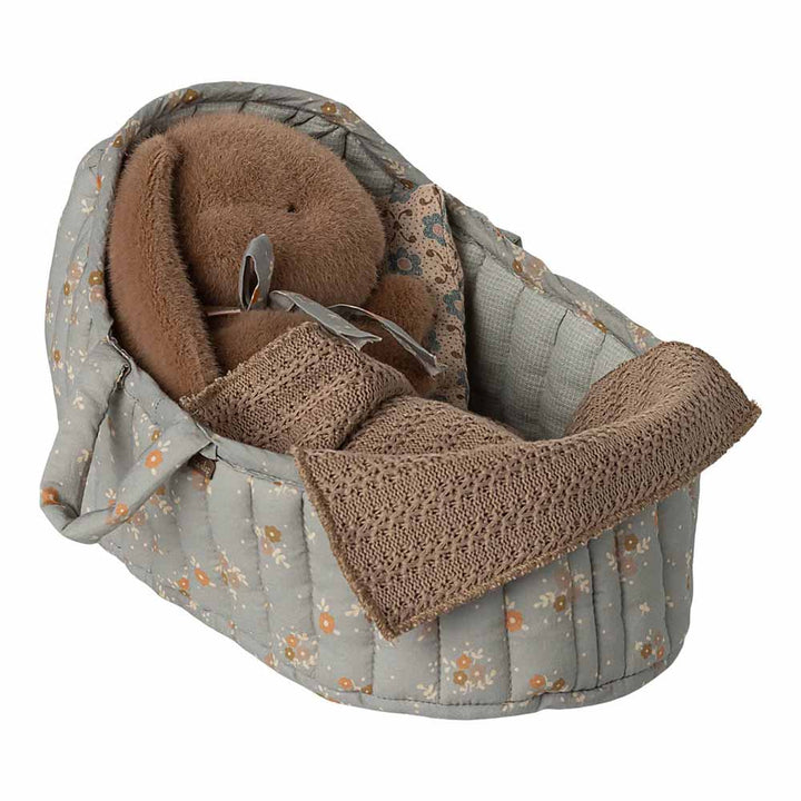 Die Maileg - Tragetasche Groß ist eine weich gepolsterte Puppentasche mit einer braunen Decke und einem Plüschbären im Inneren, die außen mit einem grauen Blumenmuster versehen ist.