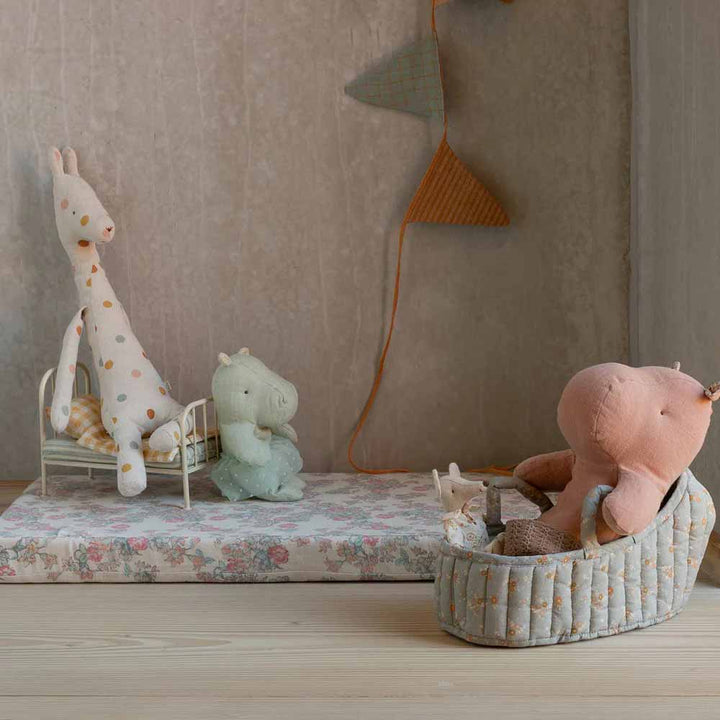 Eine Maileg - Tragetasche Groß wird mit drei Plüschtieren - einer Giraffe, einem Nilpferd und einem Schwein - auf einem geblümten Podest mit Spielzeugbetten und pastellfarbenen Dekorationen in einem sanft beleuchteten Raum ausgestellt.
