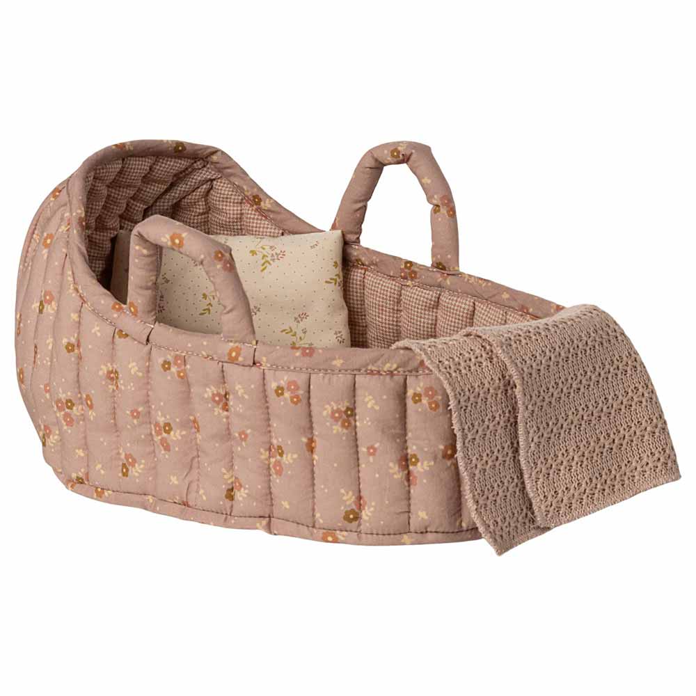 Die Maileg - Tragetasche Groß ist eine gesteppte Puppenwiege aus rosafarbenem, geblümtem Stoff mit zwei Griffen, einem kleinen Kissen und einer gestrickten beigen Decke, die über die Seite drapiert ist.