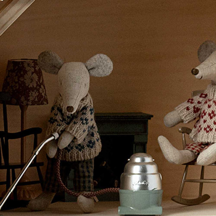 Stoffmausspielzeug in Pullovern sitzt neben einem Miniatur-Staubsauger von Maileg - Puppenmöbel.