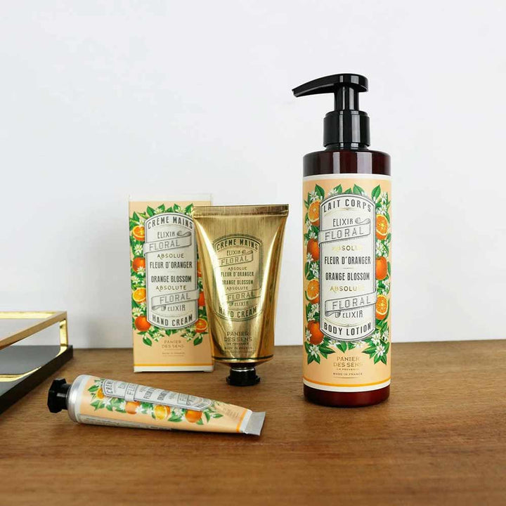 Ein Set mit blumig duftenden Hautpflegeprodukten, darunter Panier des Sens - Bodylotion Orangenblüte 250 ml, Handcreme und Handbalsam, präsentiert auf einer Holzoberfläche. Die Verpackung ist im Orangenblüten-Design gestaltet.