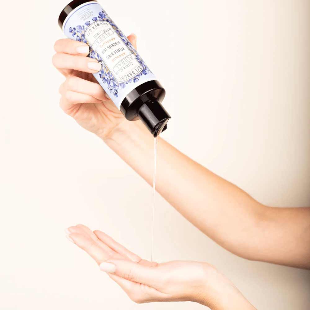 Eine Hand gießt Flüssigkeit aus einer Flasche mit schwarzem Deckel und dem blau-weißen Etikett „Panier des Sens – Duschgel Irisblütenblätter 250 ml“ auf eine offene Handfläche.