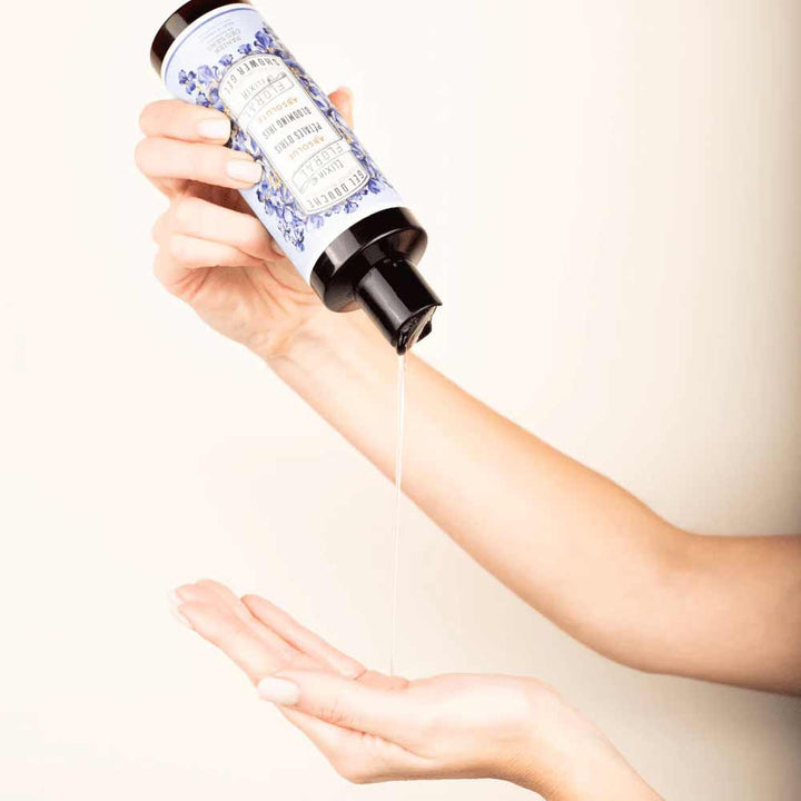Eine Hand gießt Flüssigkeit aus einer Flasche mit schwarzem Deckel und dem blau-weißen Etikett „Panier des Sens – Duschgel Irisblütenblätter 250 ml“ auf eine offene Handfläche.