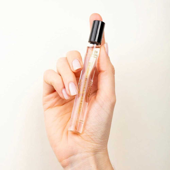 Eine Hand hält eine kleine, zylindrische Glasflasche Panier des Sens – Eau de Toilette Roll-on Irisblütenblätter 10 ml mit einer schwarzen Kappe vor einem schlichten weißen Hintergrund.