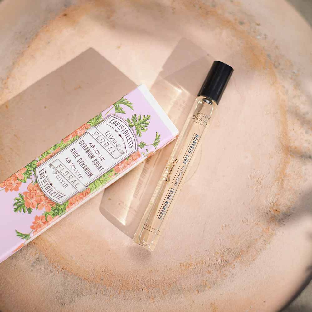 Ein Panier des Sens – Eau de Toilette Roll-on Rosengeranie 10 ml neben seiner Verpackung auf einem strukturierten Hintergrund mit der Aufschrift „Holunderblütengarten“ und Blumenmuster.