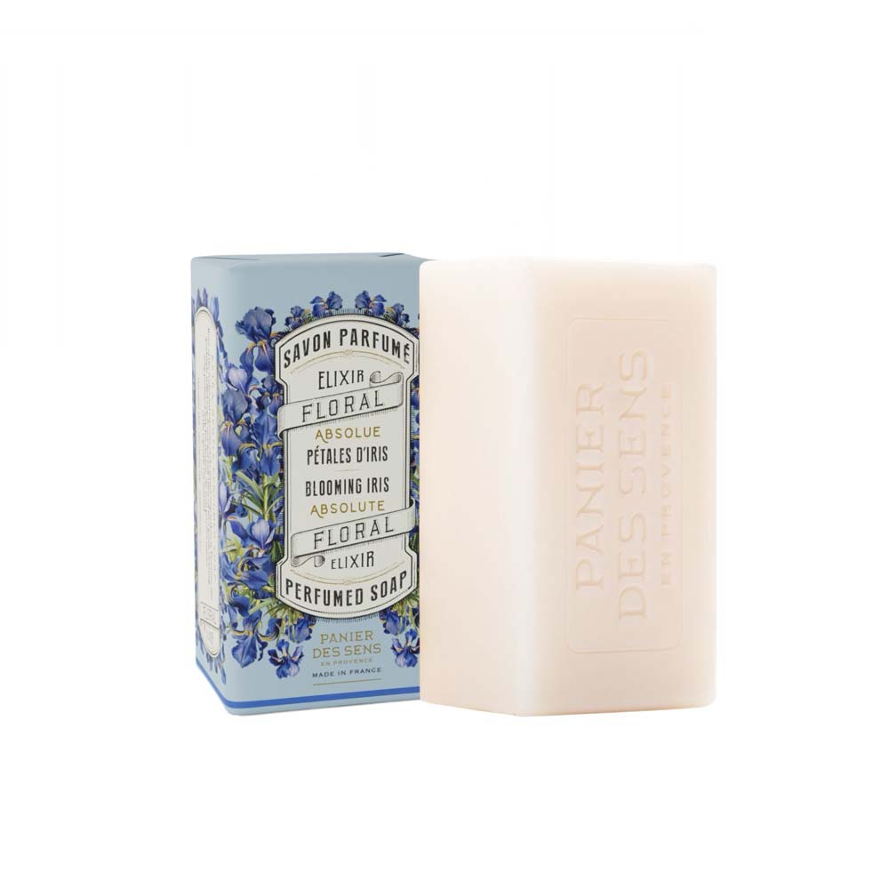 Abgebildet ist ein verpacktes Stück Panier des Sens – Feste Seife mit Duft Irisblütenblätter 150 g. Die Verpackung ist mit Blumenmotiven verziert, die unverpackte Seife ist beige und mit dem Markennamen eingraviert.