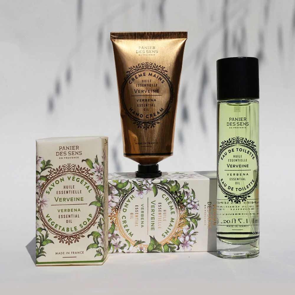 Sortiment von Panier des Sens - Handcreme Eisenkraut (Verbene) Hautpflegeprodukten mit Verpackung auf einem Hintergrund mit Schattenmuster.
