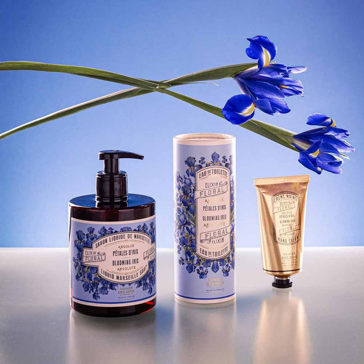 Ein Satz Panier des Sens - Handcreme Irisblüttenblätter mit einer blauen Irisblume vor blauem Hintergrund.