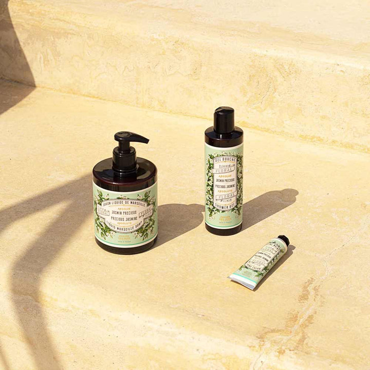 Drei Flaschen Panier des Sens - Handcreme Jasmin auf einer Betonoberfläche im Sonnenlicht angeordnet.