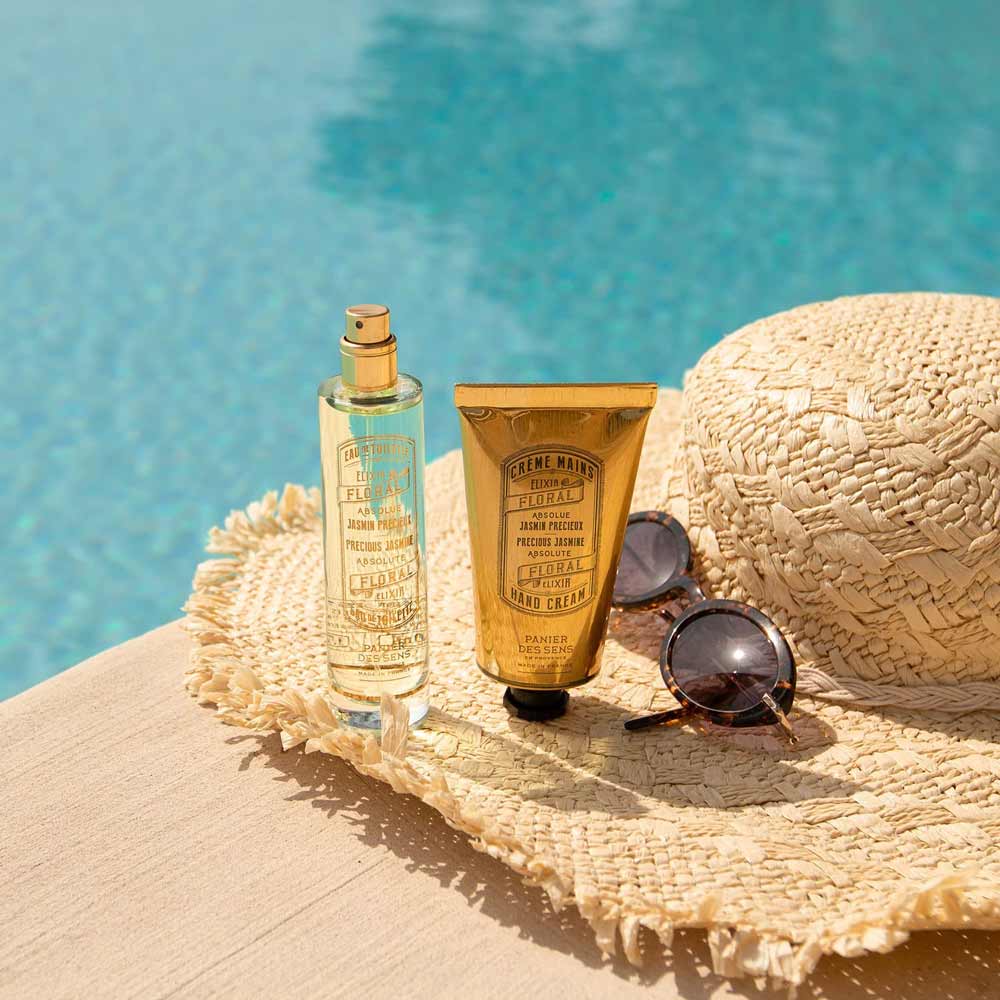 Panier des Sens - Handcreme Jasmin auf einem Strohhut neben einem Pool mit einer Sonnenbrille.