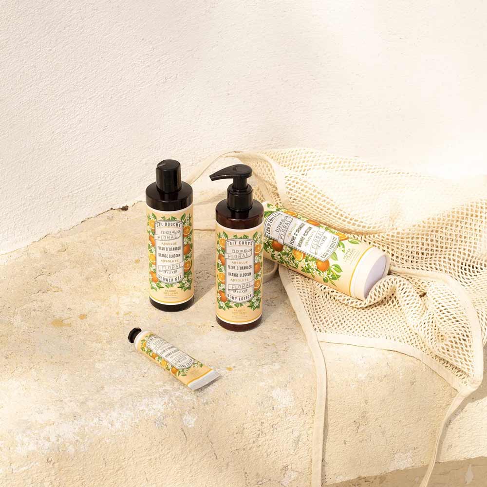 Eine Sammlung von Panier des Sens – Handcreme Orangenblüte, ausgestellt auf einer sonnigen Oberfläche neben einem Netzbeutel.