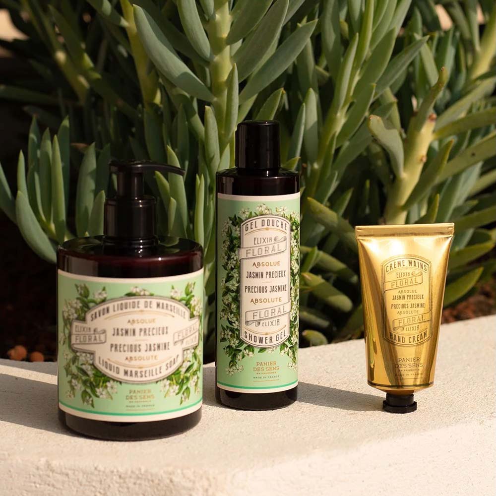 Drei Hautpflegeprodukte, darunter Panier des Sens – Marseiller Flüssige Handseife Jasmin 500 ml, ein Duschgel und eine Handcreme, werden vor einer grünen Pflanze ausgestellt. Die Produkte haben grüne Etiketten mit Blumenmustern und eine verzierte goldene Tube.