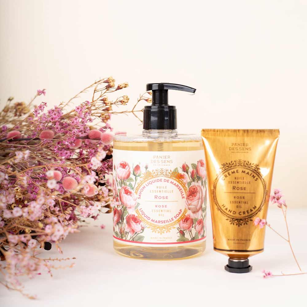 Panier des Sens - Marseiller Flüssige Handseife Rose 500 ml und eine Tube Handcreme mit Blumenmuster, neben getrockneten Blumen auf hellem Hintergrund platziert.