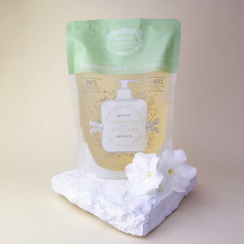 Panier des Sens - Marseiller Flüssigseife Nachfüllbeutel Jasmin 500 ml auf einem weißen Stein platziert, begleitet von weißen Blumen.