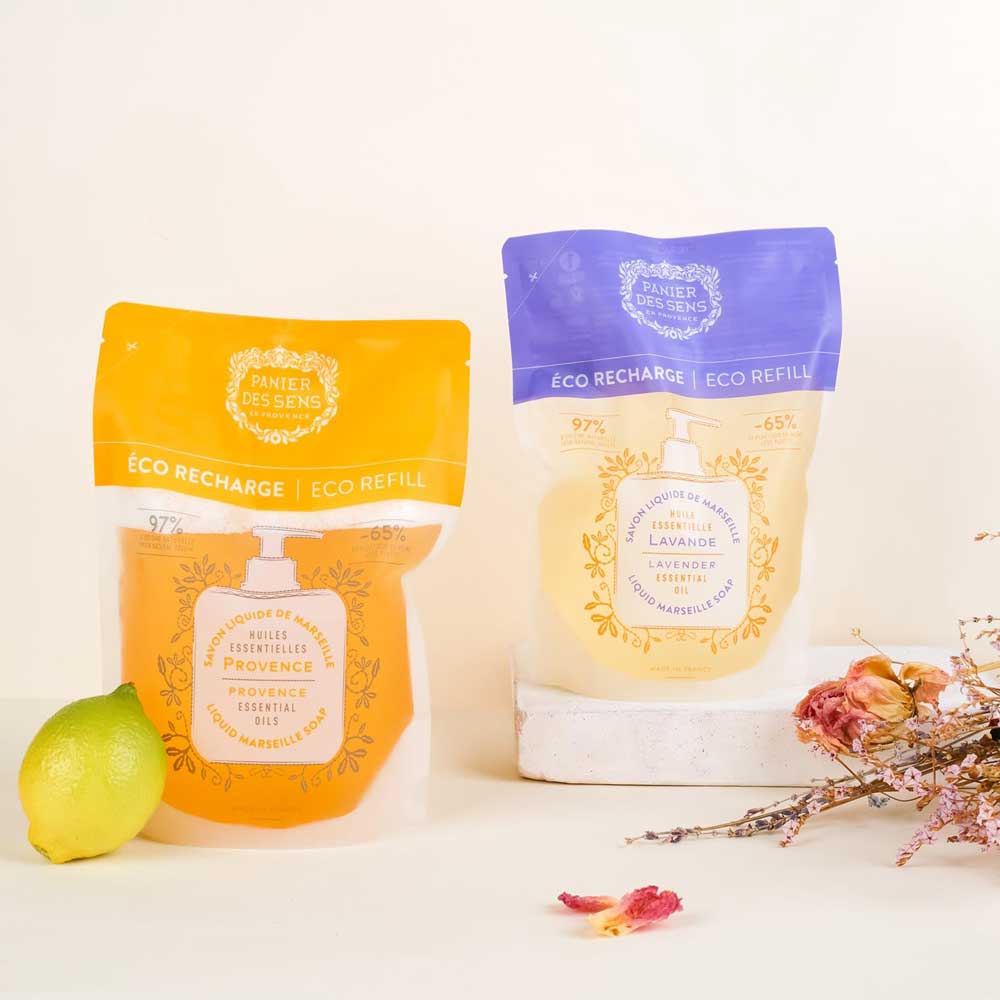 Panier des Sens - Marseiller Flüssigseife Nachfüllbeutel Provence 500 ml Nachfüllbeutel für Waschmittel, platziert vor einem neutralen Hintergrund mit einer Zitrone und getrockneten Blumen.