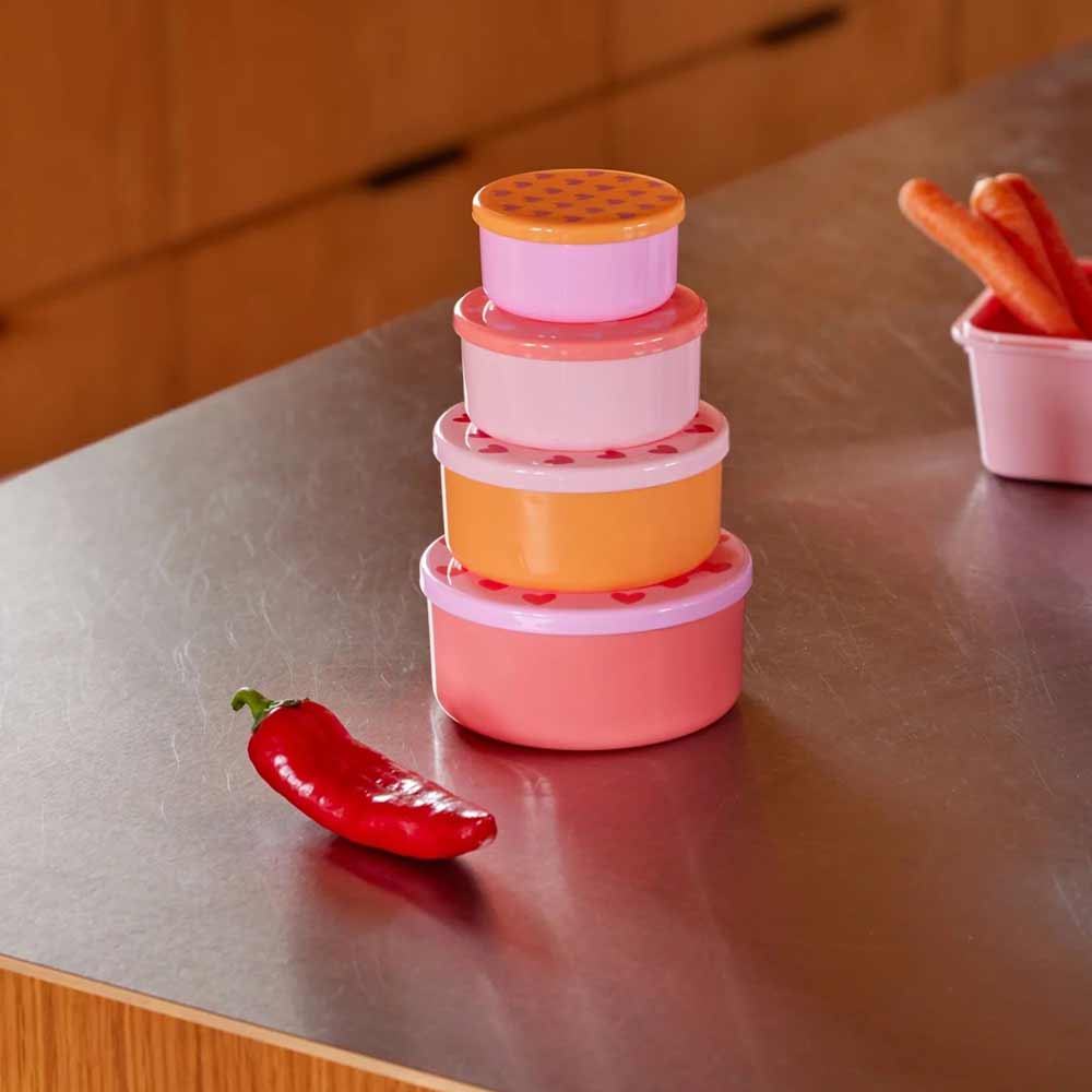 Gestapelter Reis – Lebensmittelboxen Herzen rund 4er-Set auf einer Arbeitsplatte neben einer roten Paprika und einem kleinen Behälter mit Karottensticks.