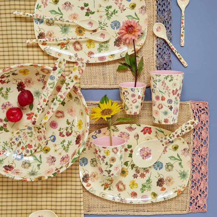 Eine Tischdekoration mit Tellern, Schüsseln, Löffeln mit Blumenmuster, Reis-Melaminbecher Floras Dream Medium und zwei Blumen in Bechern. Zwei Radieschen befinden sich in einer Schüssel, darunter karierte und gewebte Tischsets.