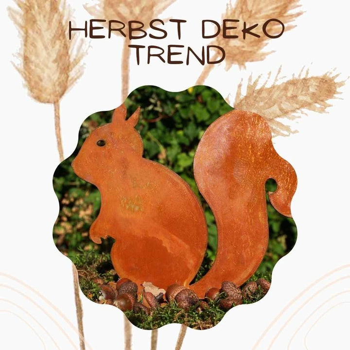 Das Rostikal - Metalldeko Rost Eichhörnchen Kecki ist eine trendige Herbstdekoration aus rostigem Metall, umgeben von Eicheln, mit "HERBST DEKO TREND"-Schriftzug und getrocknetem Gras im Hintergrund.