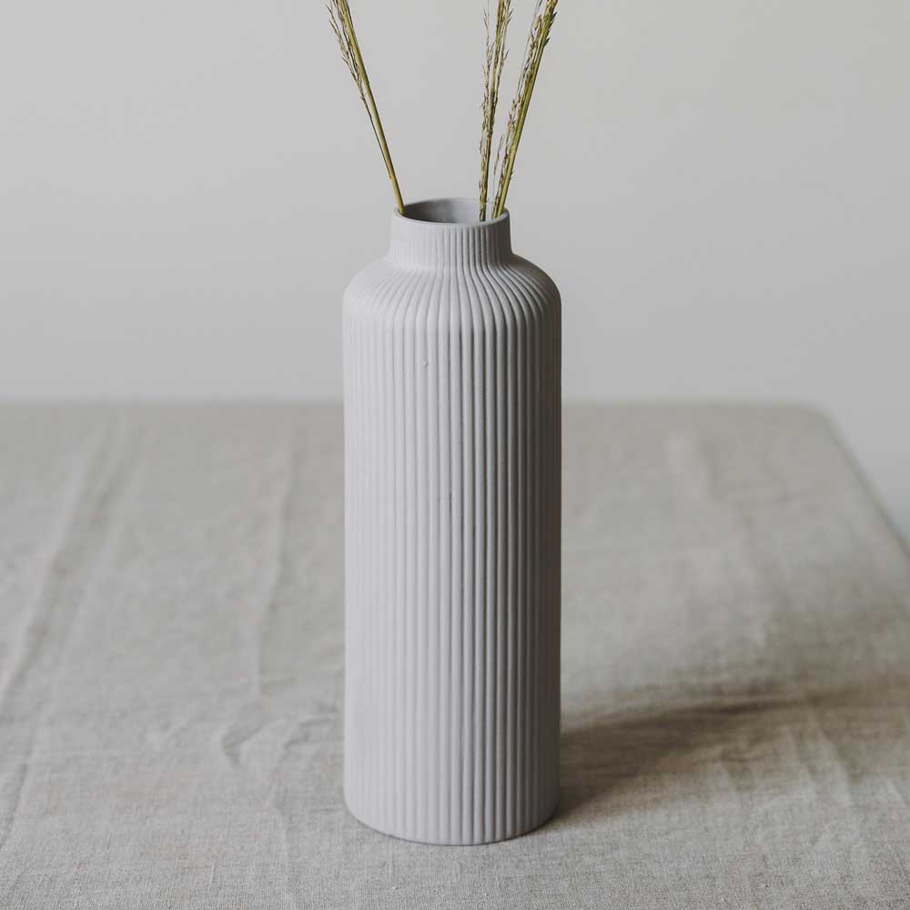 Die Storefactory Ådala Vase Keramik im hohen grauen Rippendesign hält zwei getrocknete Grashalme auf einer hellen Tischdecke.