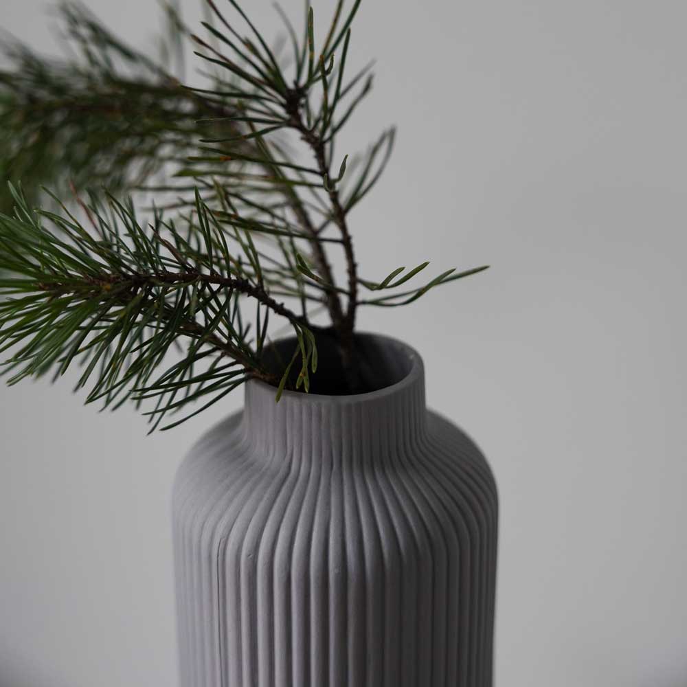 Die Ådala Vase Keramik in Grau von Storefactory hält Kiefernzweige vor einem hellen Hintergrund.