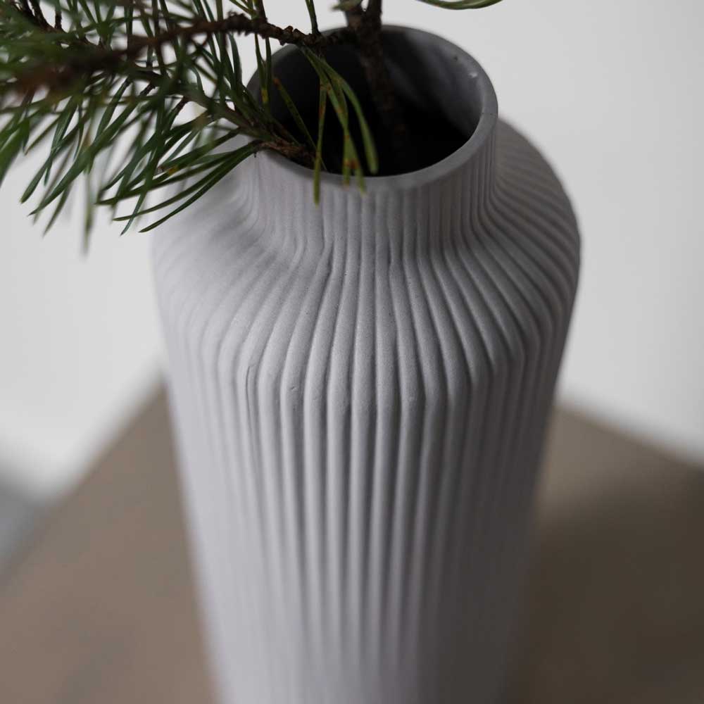Nahaufnahme der Storefactory – Ådala Vase Keramik, eine hohe, gerippte, graue Vase, gefüllt mit Kiefernzweigen und auf einer glatten Oberfläche platziert.
