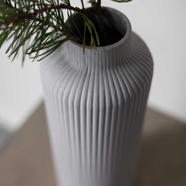Nahaufnahme der Storefactory – Ådala Vase Keramik, eine hohe, gerippte, graue Vase, gefüllt mit Kiefernzweigen und auf einer glatten Oberfläche platziert.