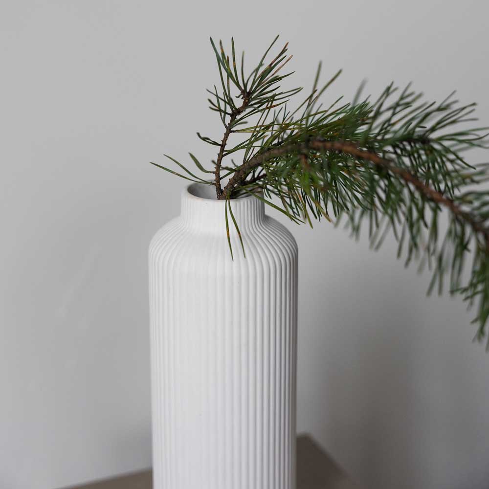 Storefactory – Ådala Vase Keramik mit weißem Rippendesign hält einen einzelnen Kiefernzweig vor einem einfachen Hintergrund.
