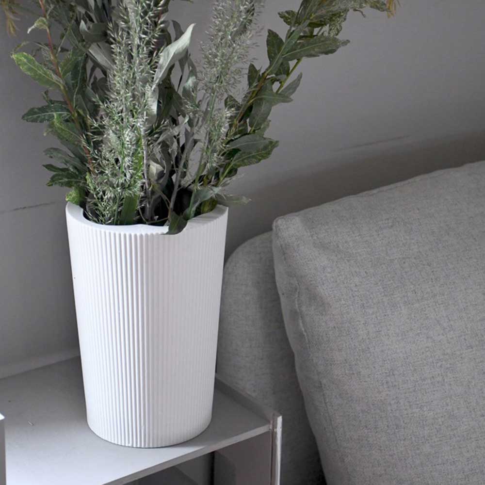 Die Eksberg-Vase mit Grünpflanzen von Storefactory steht auf einem kleinen Tisch neben einem grauen Sofa.