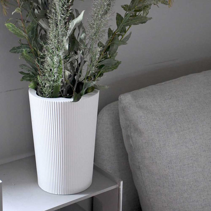 Die Eksberg-Vase mit Grünpflanzen von Storefactory steht auf einem kleinen Tisch neben einem grauen Sofa.