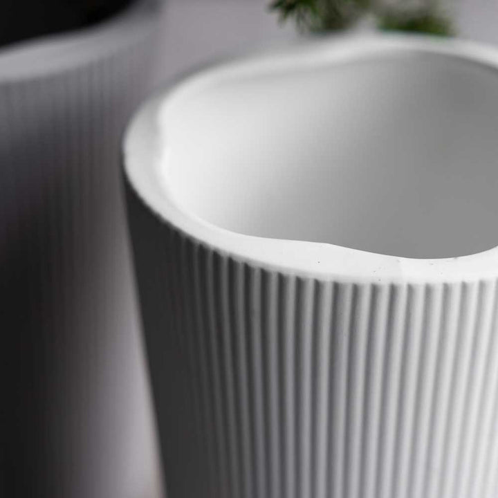 Nahaufnahme einer Storefactory-Eksberg-Vase, einer weißen zylindrischen Vase mit vertikalen Rillen, neben einem dunkleren zylindrischen Objekt.