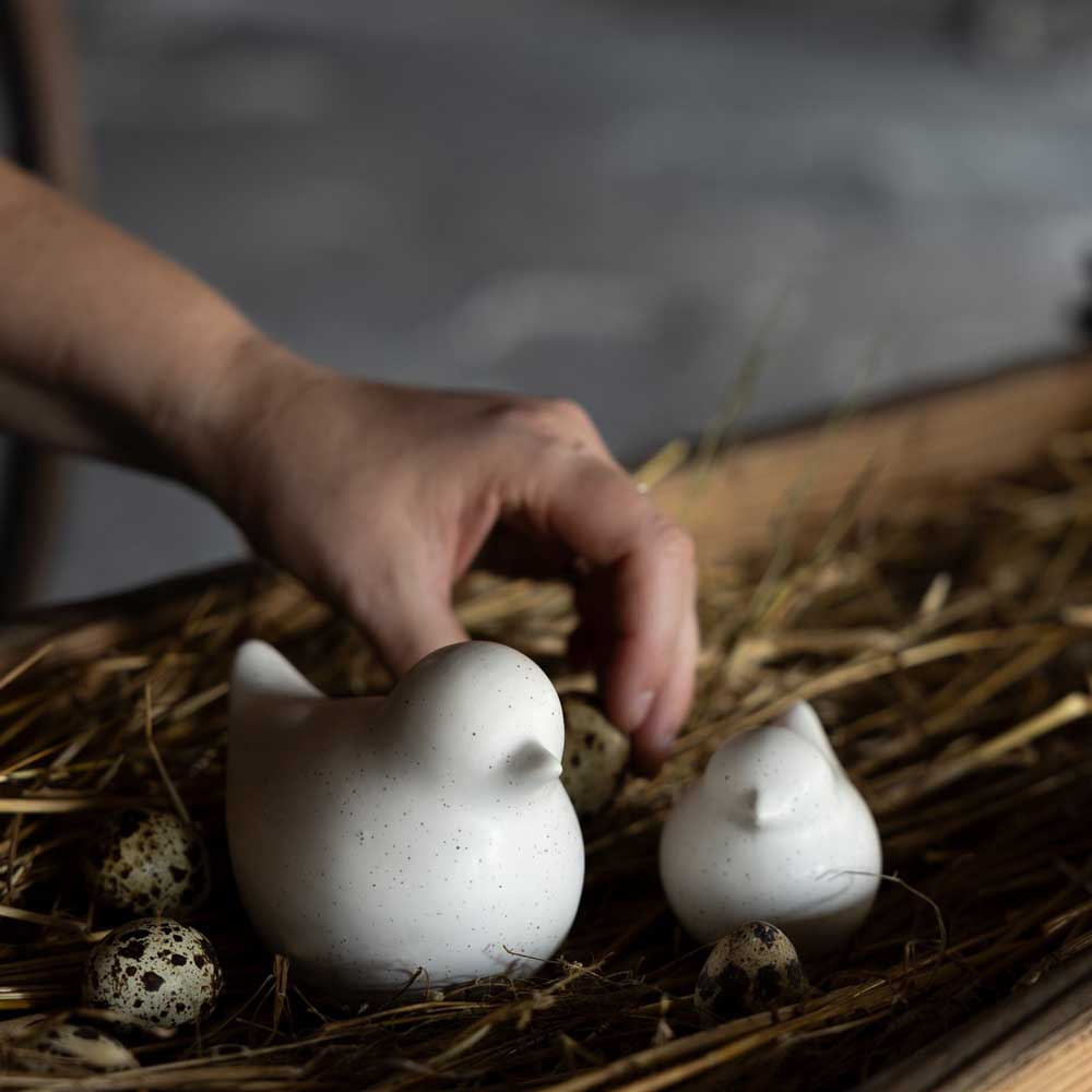 Wachteleier arrangieren mit den weißen Vogelskulpturen aus Keramik auf Stroh von Storefactory Ellen Huhn.