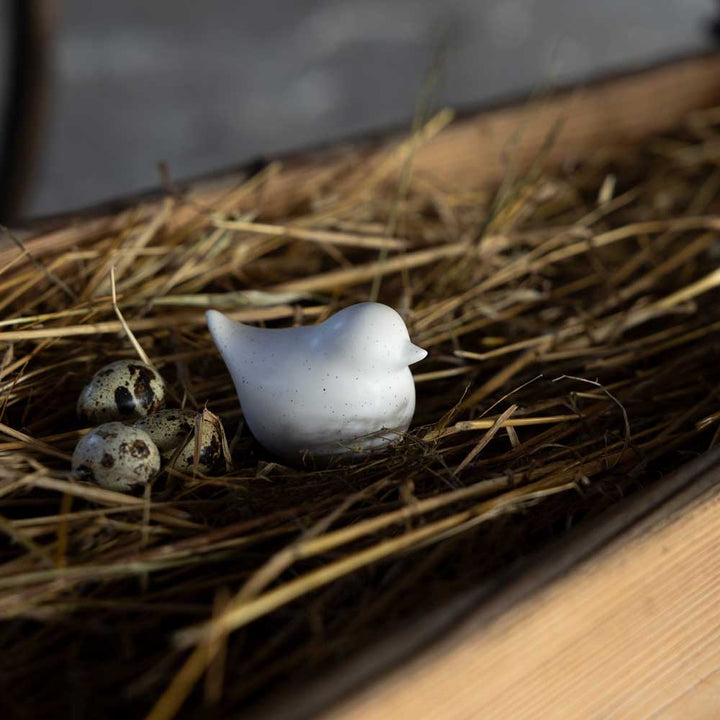 Die Storefactory Ellen Huhn zeigt einen kleinen Keramikvogel mit drei Wachteleiern, die auf Stroh in einem Holztablett nisten.