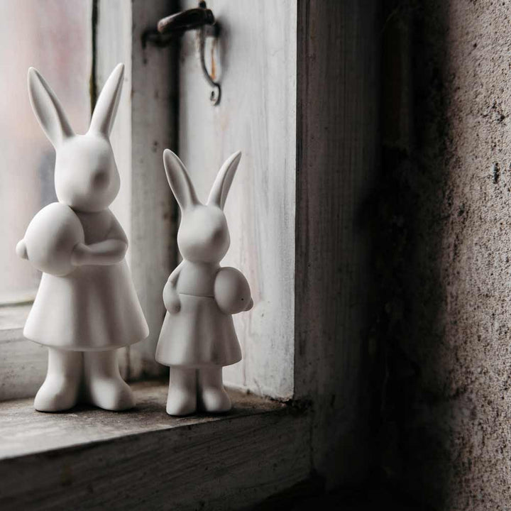 Zwei Storefactory - Ester Hase-Figuren an einem staubigen Fenster.