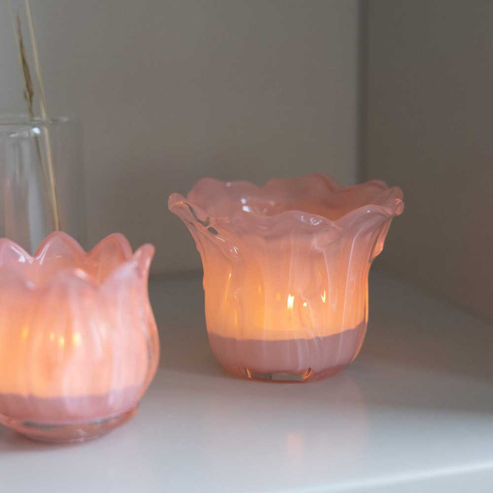 Zwei Storefactory - Ljunga Teelichthalter aus rosa geriffeltem Glas, jeweils mit einer brennenden Kerze darin, stehen auf einem Regal.