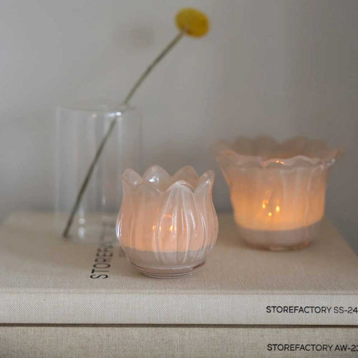 Zwei beleuchtete Storefactory - Ljunga Teelichthalter auf gestapelten Büchern, mit einem einzelnen Blumenstiel in einem Glas daneben.