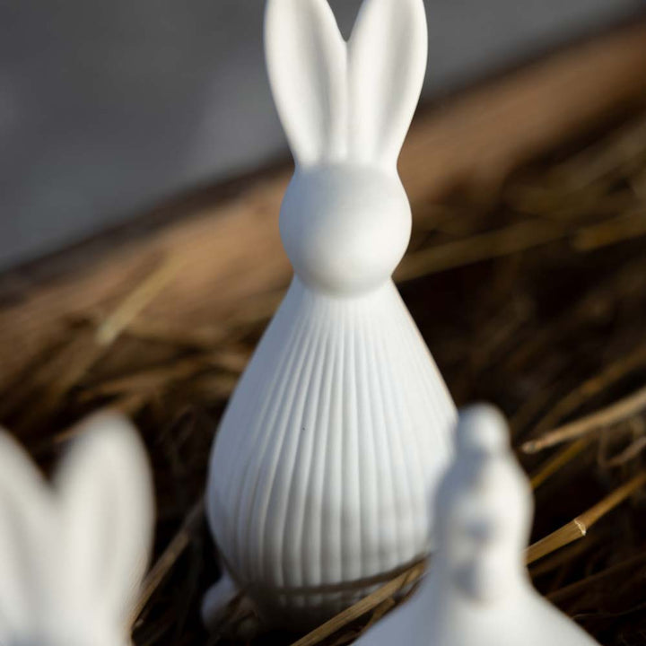 Der Selma Hase von Storefactory ist eine Hasenfigur aus Porzellan, die auf einem Strohbett präsentiert wird.
