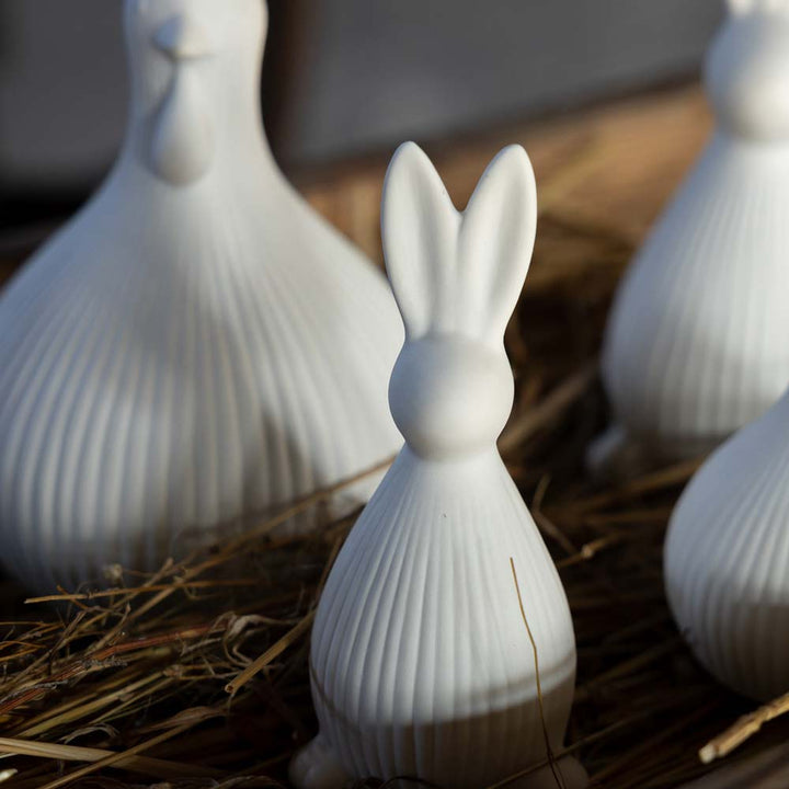 Die Storefactory Selma Hase zeigt weiße Keramikfiguren eines Kaninchens und eines Huhns auf einer Strohoberfläche, aufgenommen in natürlichem Licht.