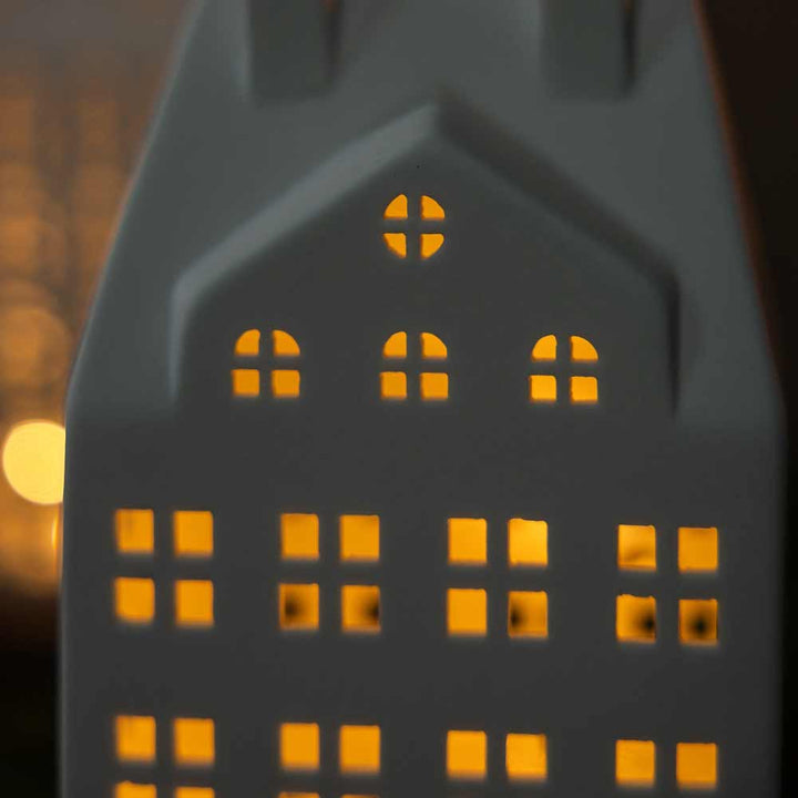 Das Storefactory – Storstaden Nr. 2 Lichthaus Deko ist ein kleines, weißes Keramikhaus mit Fenstern, die durch die Innenbeleuchtung warm strahlen und so im Dunkeln eine gemütliche Atmosphäre schaffen.